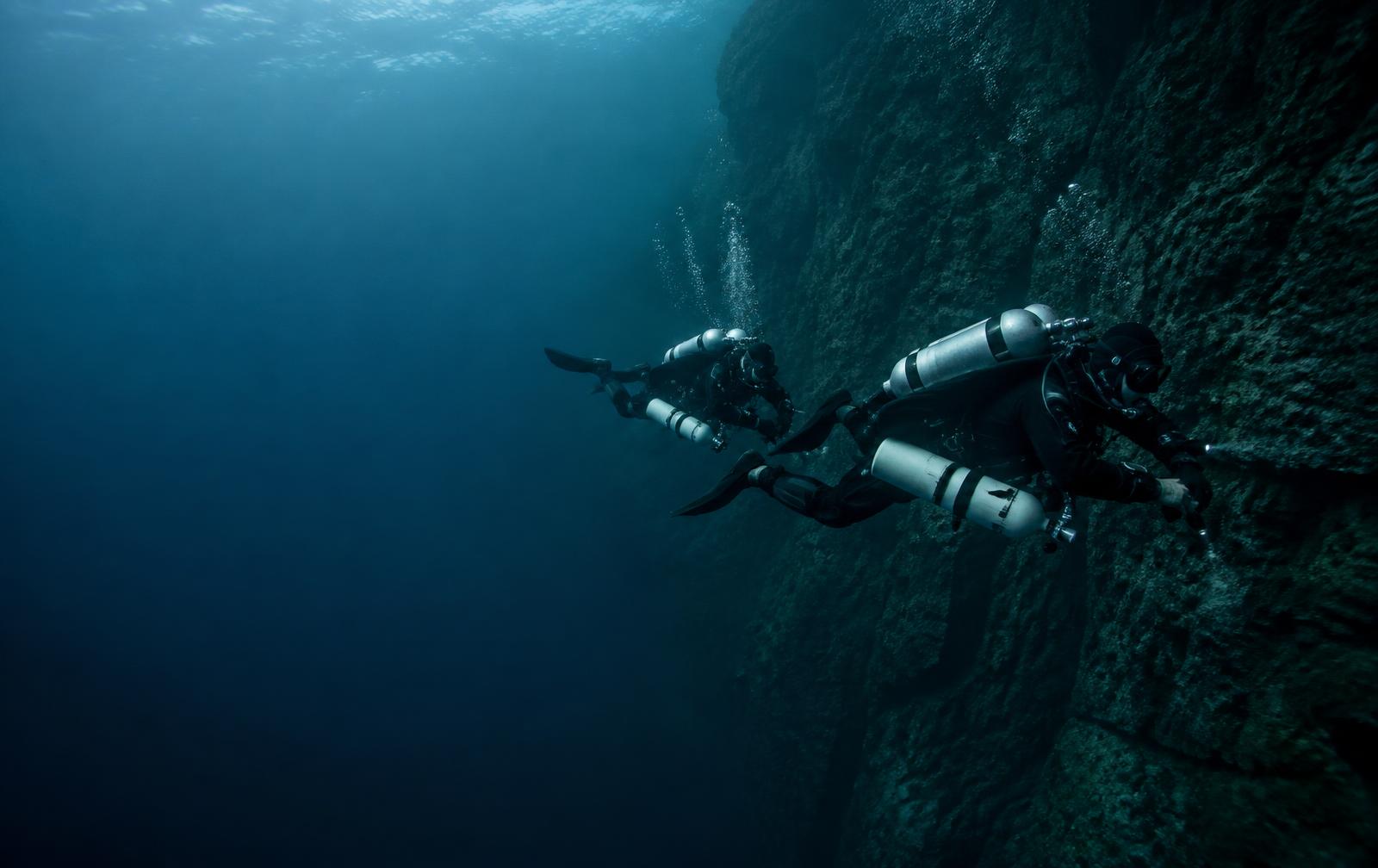 Technical dive team descending beside a deep rock wall